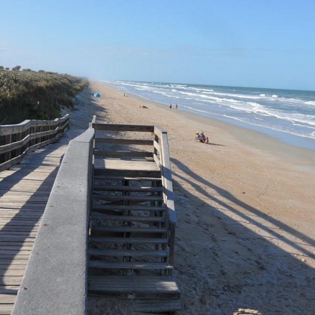Sandy beach with boardwalk sloping to sand in front of dune grass