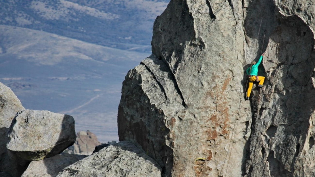 A colorful female climber ascends granite rock called the Anteater in City of Rocks National Reserve