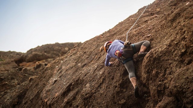 Ground view of a female rock climber ascending a cliff face above