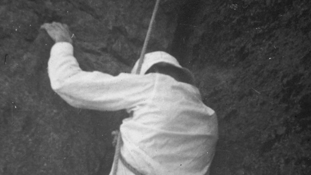 A man with a rope tied around his waist climbing Devils Tower in 1937