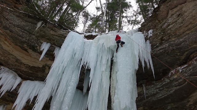 A climber working his way up a frozen water fall, ice climbing.