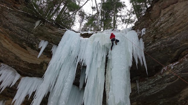 A climber working his way up a frozen water fall, ice climbing.