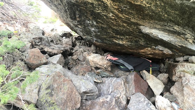 Bouldering crash pads left laying underneath a boulder, considered trash.