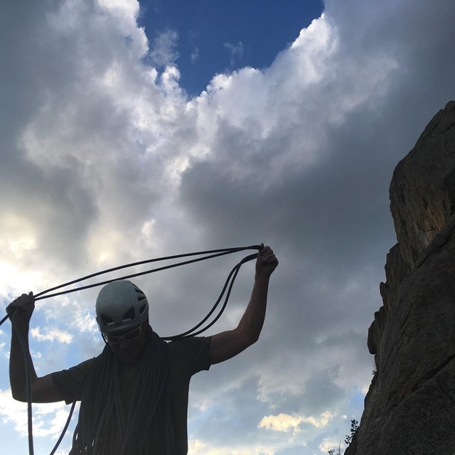 Man coiliing a climbing rope shaded by the setting sun.  