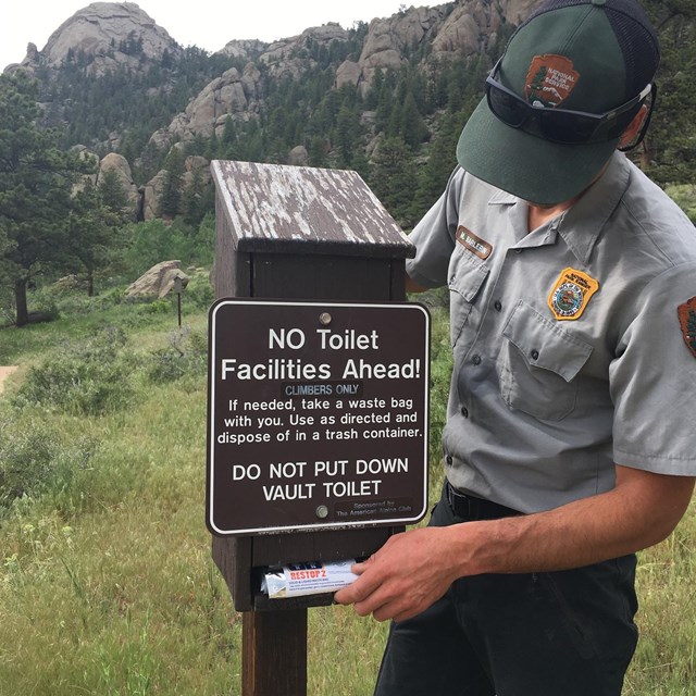 Climbing Ranger stocking a Wag Bag dispenser at a climbing access trail