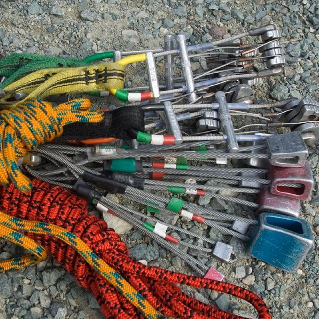 Photo of Traditional Climbing equipment; slings, cams and nuts laying on the ground in a bundle. 