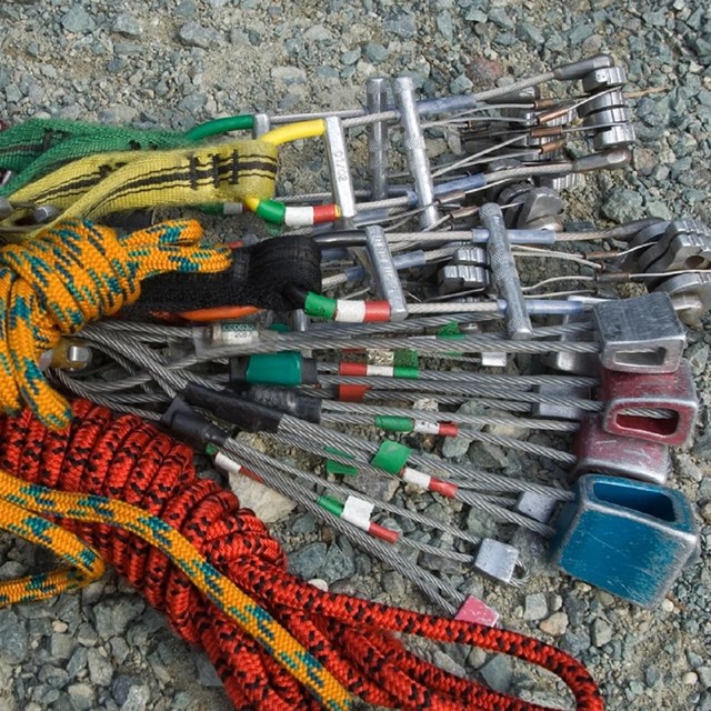 Photo of Traditional Climbing equipment; slings, cams and nuts laying on the ground in a bundle. 