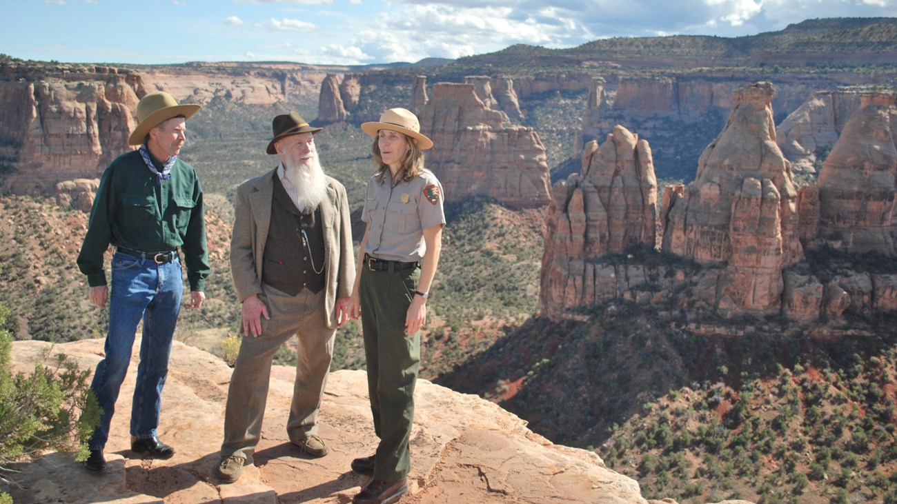 three uniformed adults stand at the edge of an expansive canyon