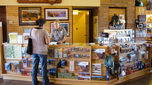 ranger at desk speaks with visitor, desk is covered in purchasable items from gift shop