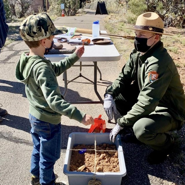 ranger sits with jr ranger holding up artifacts