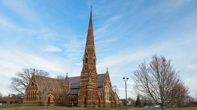 A church with green grass and bare trees in front against a blue sky. 