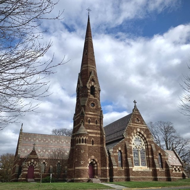 A colorful stone church with a rising steeple and stained glass windows. 