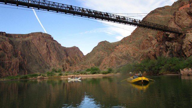 people rafting on a river and riding horseback across a bridge