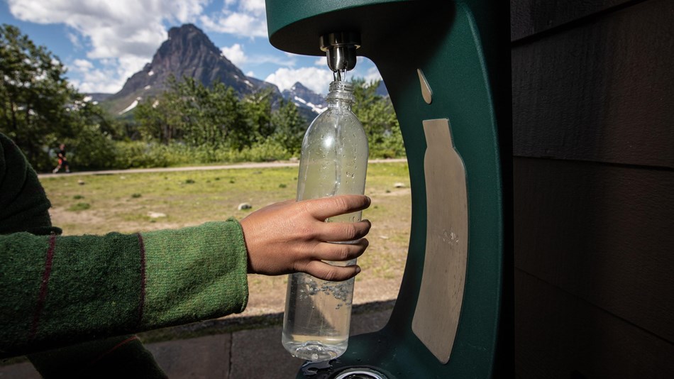 person refills water bottle at a bottling station with mountain in the background