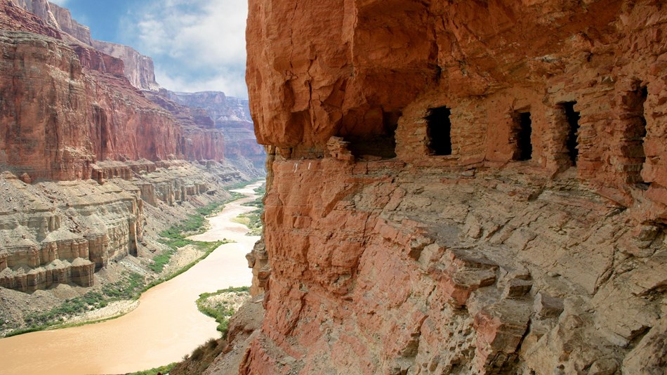 calm brown river flows below prehistoric cliff dwellings