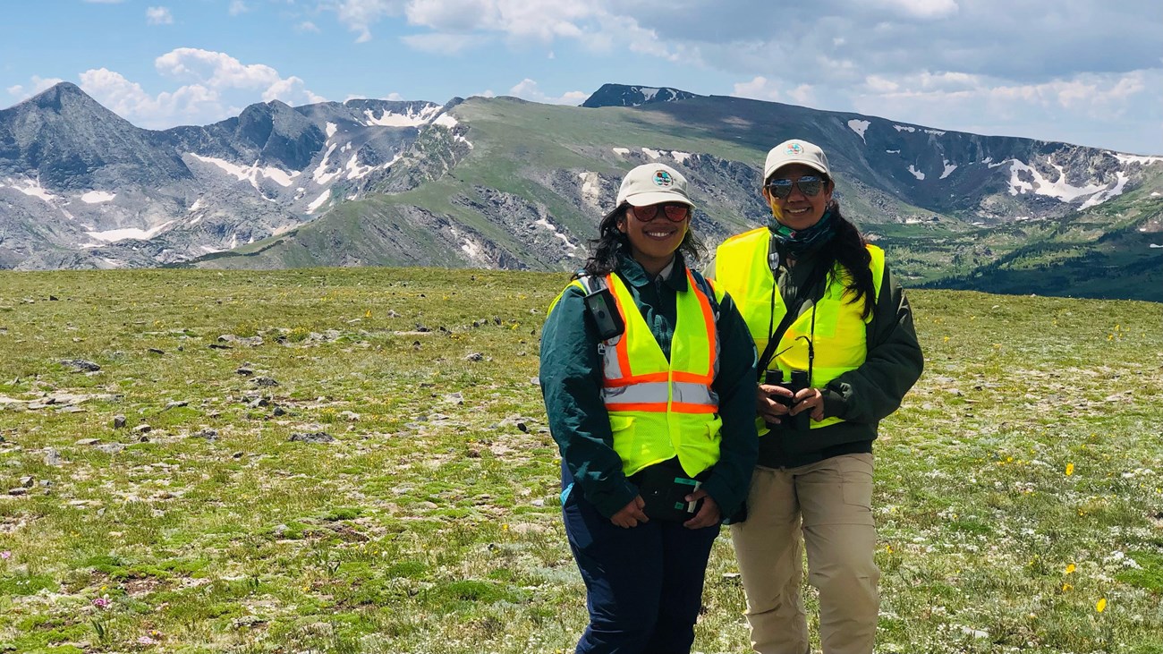 Two people stand in yellow safety vests on the alpine tundra. 