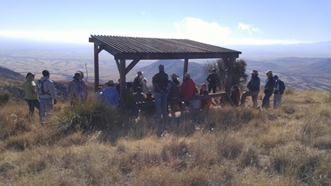A ranger speaks to a group on a grass covered mountain peak