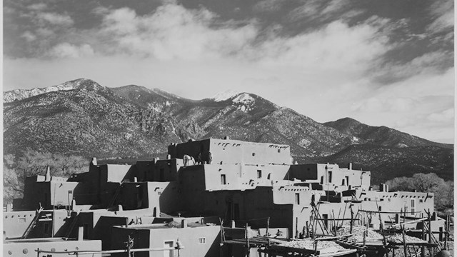 A stone and adobe building with snow covered mountains in the background