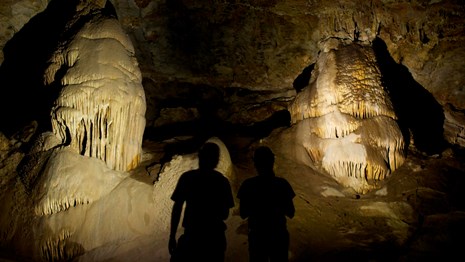 Visitors silhouetted in flashlight beams, cave formations illuminated