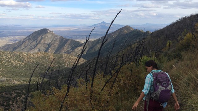 A hiker on a trail, mountains and valleys in the distance.