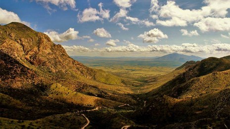 A wide canyon with peaks flanking either side and mountains in the distance