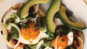 A plate of eggs on tortillas with avocado, beans, onion, and tomato