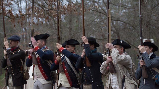 Reenactors stand with musekts.
