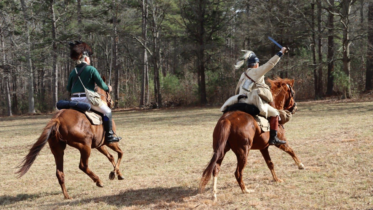 Two riders on horseback with swords drawn. 