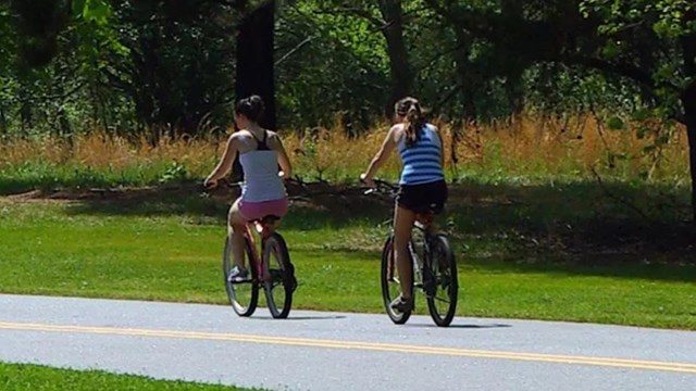 Two visitors ride bikes on road