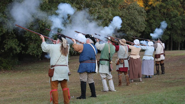 Line of reenactors fire muskets. 
