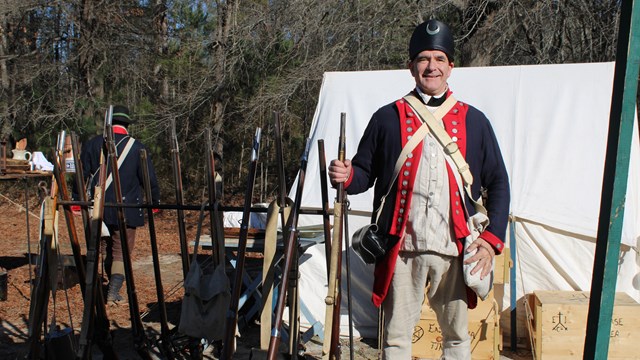 Image of reenactor holding a musket next to a stack of muskets.