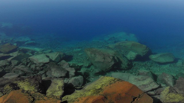 The rocky underwater near shore of Wizard Island and colors from light waves