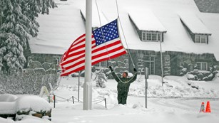 A ranger raises the US flag in a snowstorm.