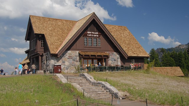 Stone steps, a grassy meadow, and a 2-story, multi-pitched historic building of stone and wood