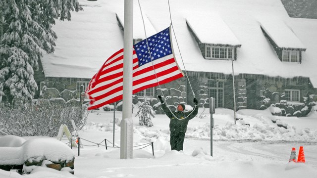 A ranger raises the US flag in a snowstorm.