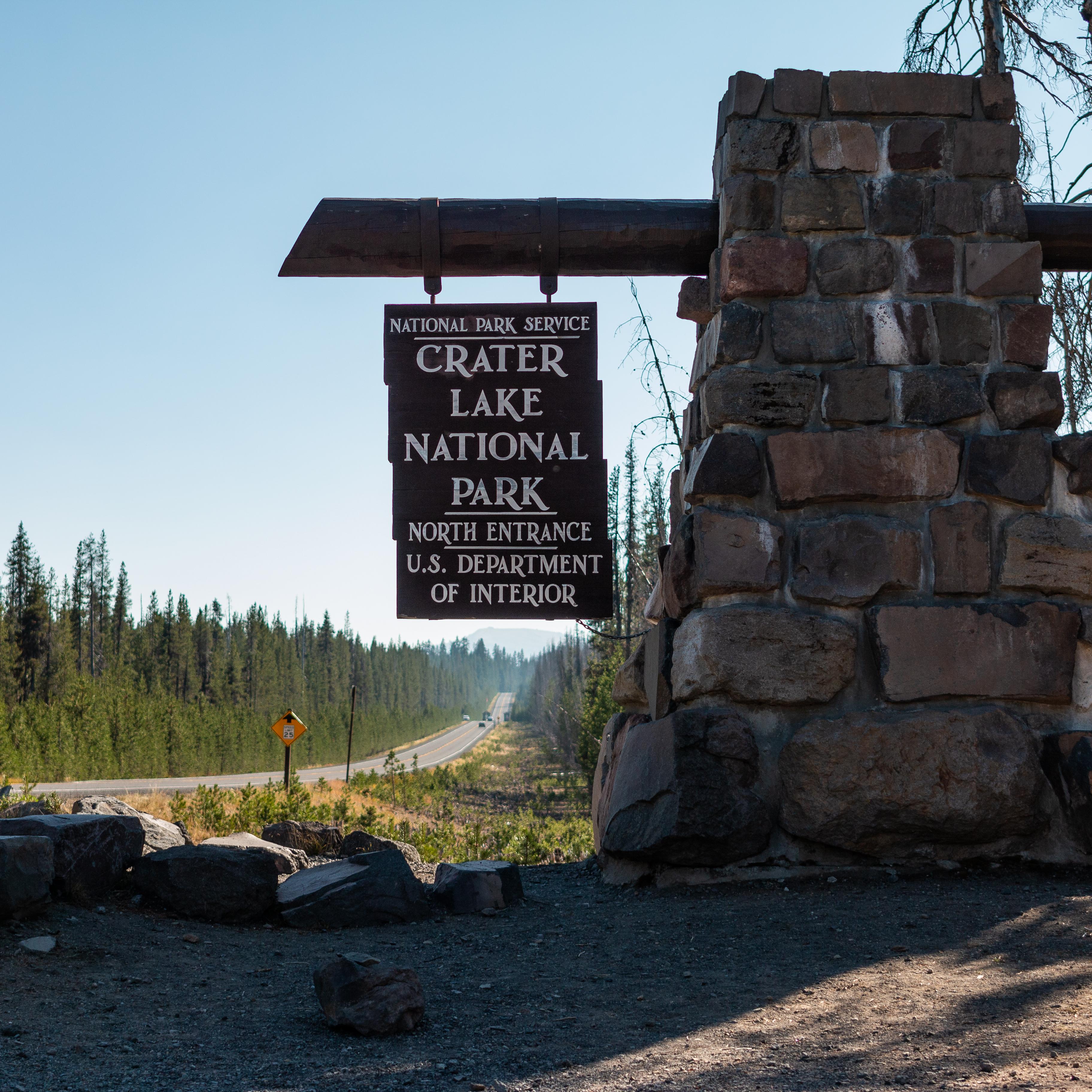 North Entrance sign has white letters hangs from a wooden beam on a stone pillar.