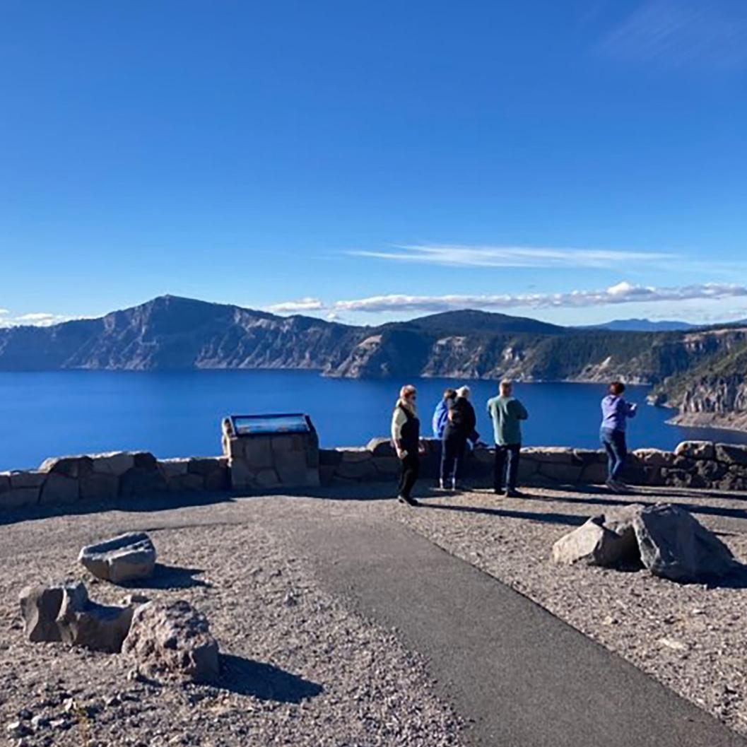 An exhibit set in a short stone wall at the end of a long sidewalk where people look at a blue lake.