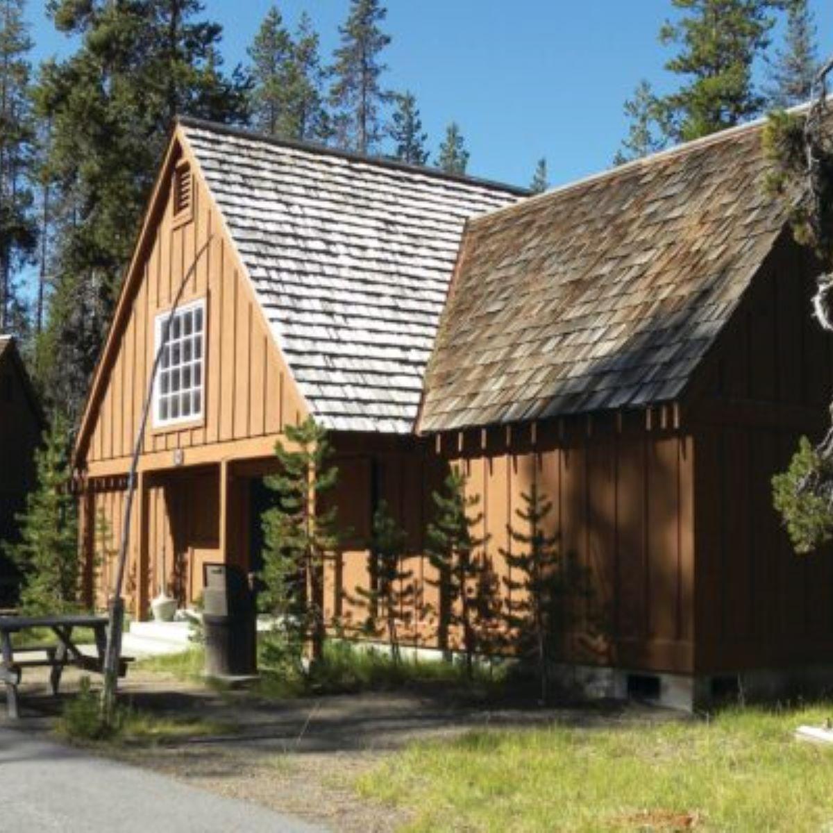 Cabin F has a high pitched wood-shingled roof is brown with picnic tables and pine trees
