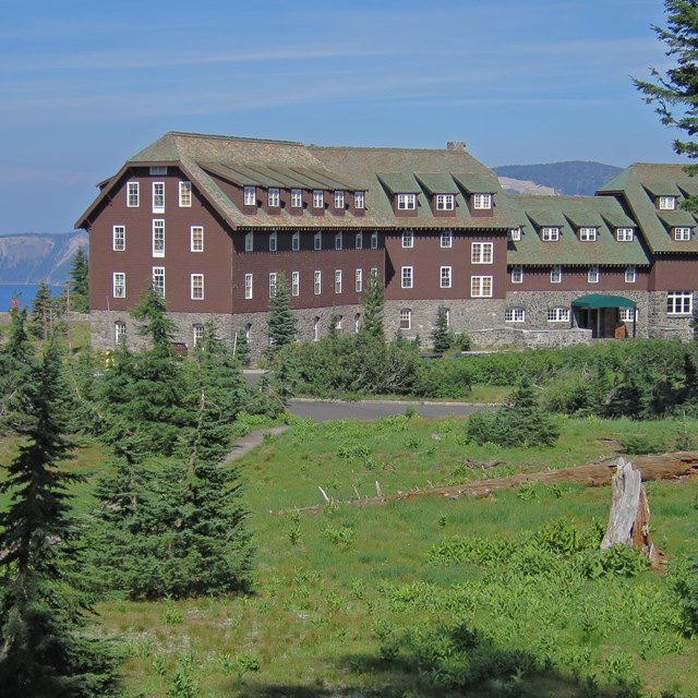 Crater Lake Lodge sits between Crater Lake and a green meadow with trees.