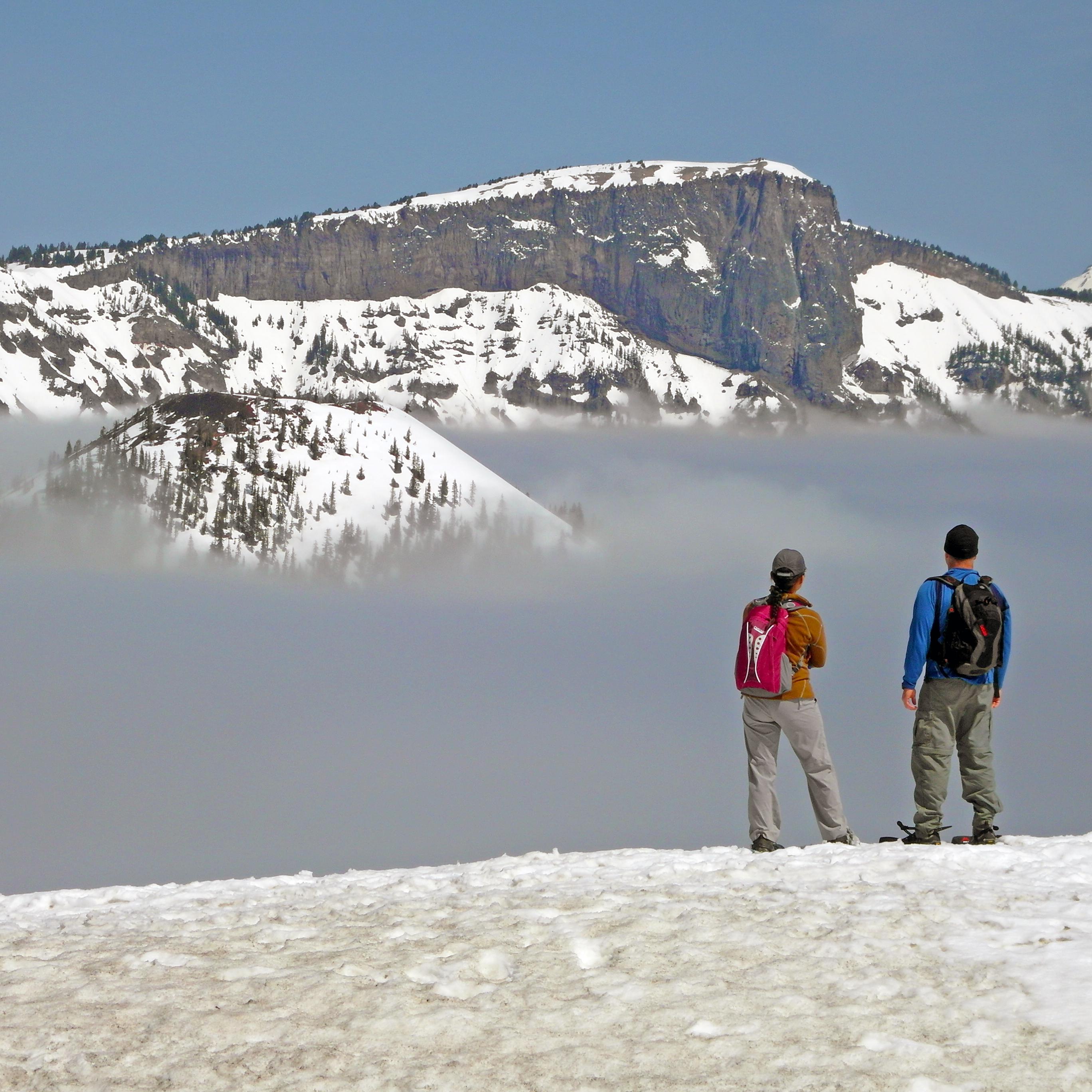 Two snowshoers gaze at the lake, filled with fog.