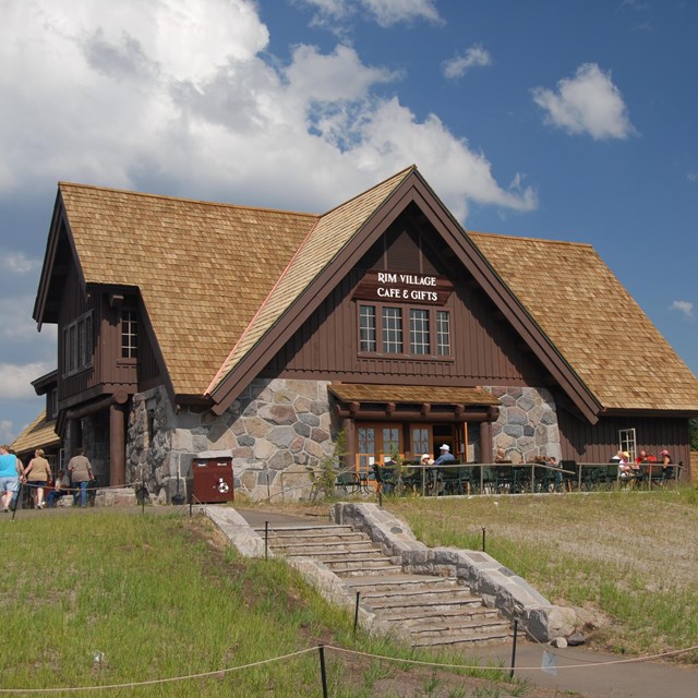 Stone steps, a grassy meadow, and a 2-story, multi-pitched historic building of stone and wood