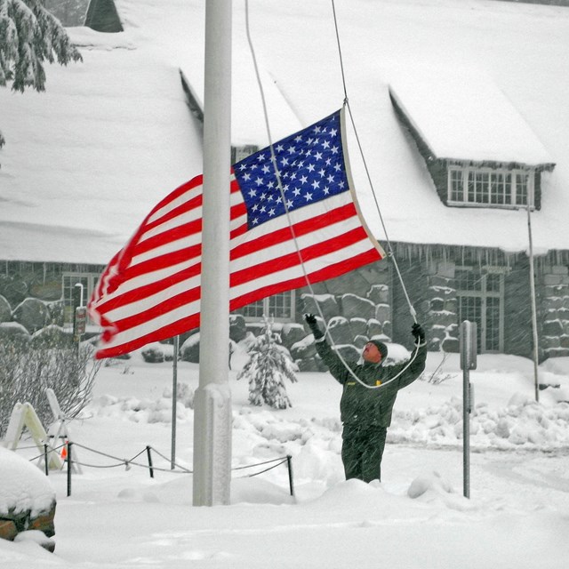 A ranger raises the US flag in a snowstorm.
