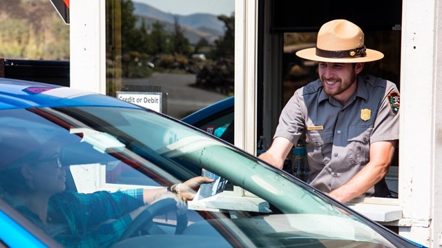 A ranger at the entrance booth hands a brochure to a visitor.