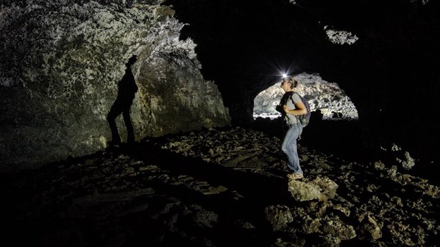 A woman with a headlamp stands inside a cave.