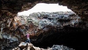 A visitor stands inside a lava tube, under a large opening to the surface