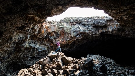 A visitor stands inside a lava tube under a large opening to the sky.