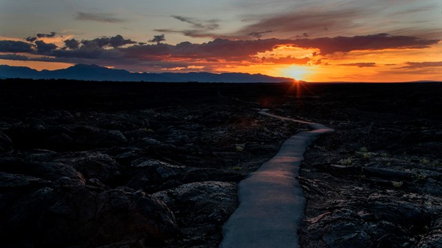 sunrise over a winding path crossing a dark, rocky landscape