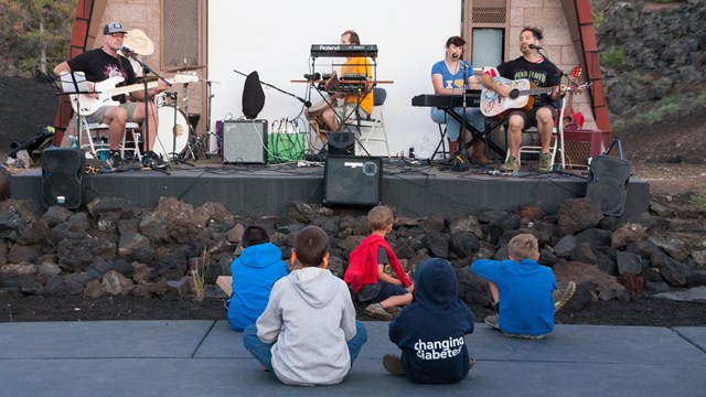 several children sitting in front of a band playing on a stage