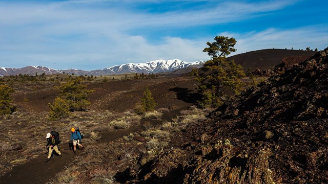 Two hikers with large backpacks traverse the volcanic landscape.