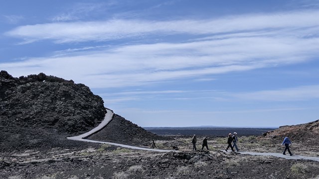 Visitors walk along a paved trail to and from a small spatter cone.